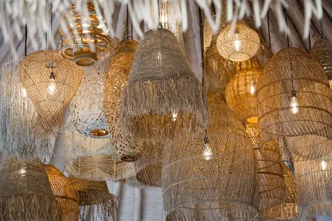 Close view of many lit woven rattan lampshades with fringes hanging together.