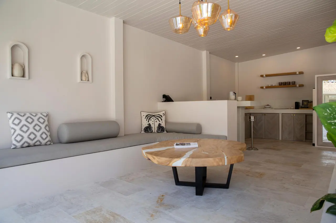 Lounge with a built-in grey sofa, a round wood-slab coffee table under an amber glass chandelier, arched wall niches and the kitchen counter.
