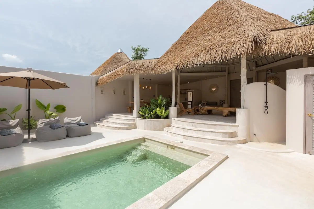 Plunge pool in front of the thatched open sala with curved stone steps and an outdoor shower, and bean-bag loungers under a parasol at left.