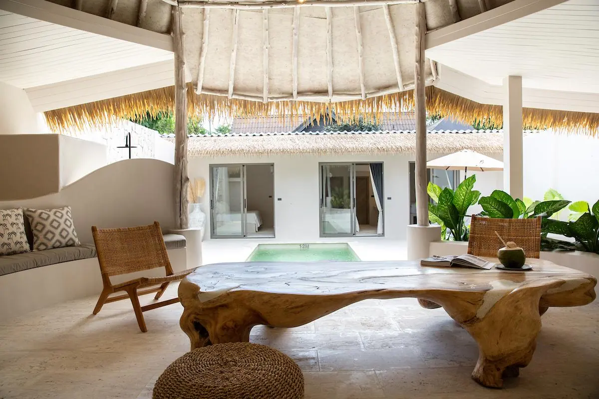 Thatched living sala with a teak-root coffee table, a coconut drink and rattan chairs, looking out over the plunge pool to the bedroom wing.
