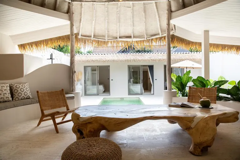 Thatched living sala with a teak-root coffee table, a coconut drink and rattan chairs, looking out over the plunge pool to the bedroom wing.