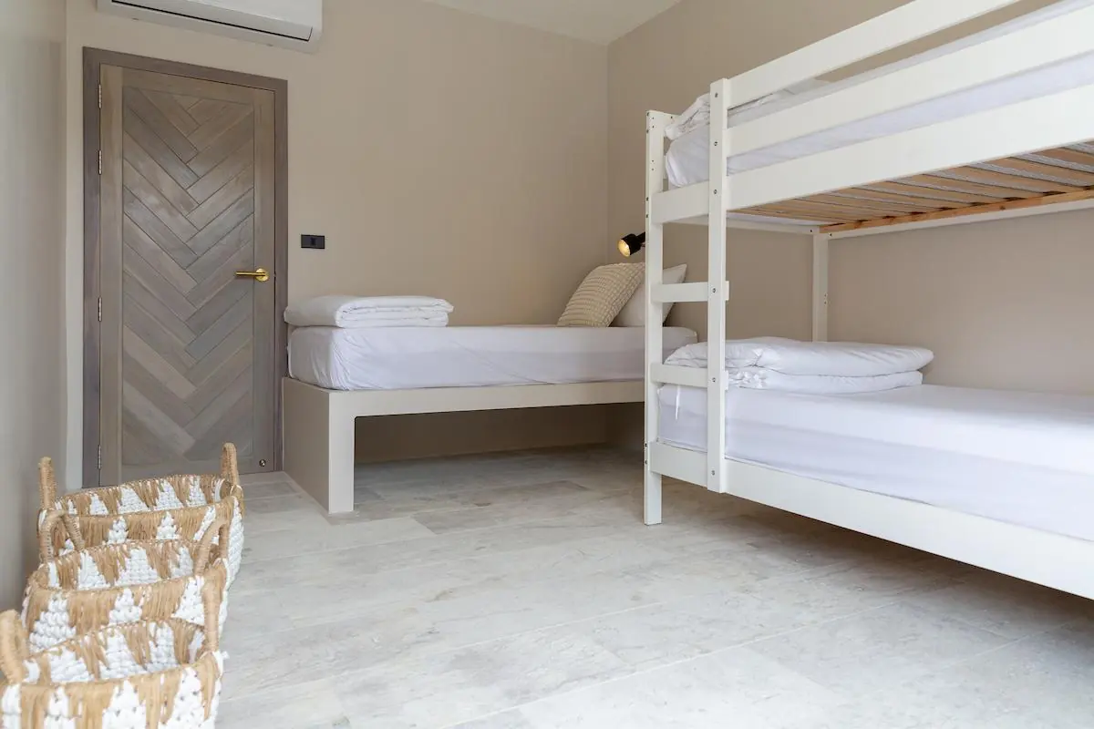 Third bedroom with a white wooden bunk bed, a single bed, woven baskets and a chevron timber door.