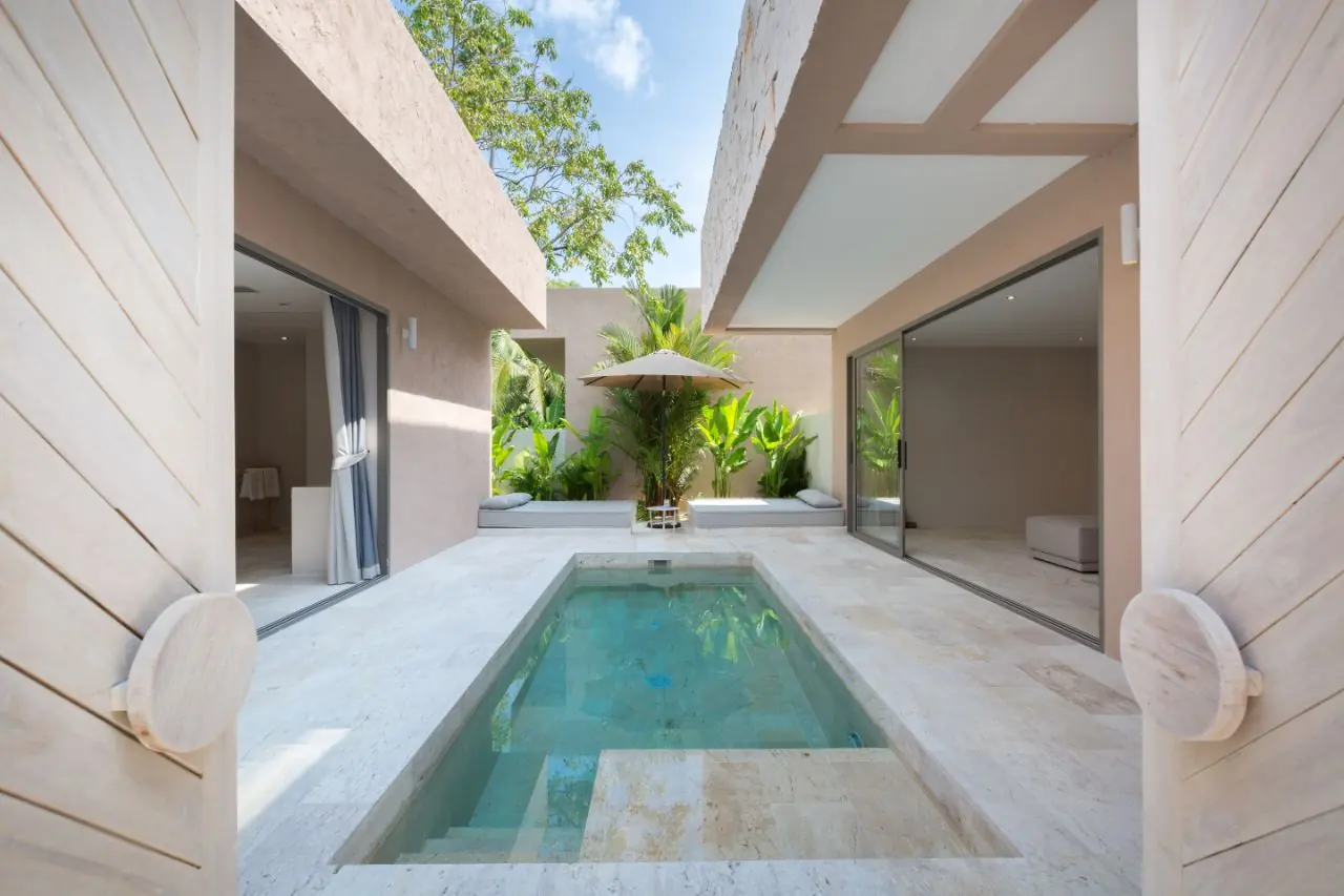 Private plunge pool in a travertine courtyard between two glass-walled rooms, seen through open chevron timber doors with round wooden handles.