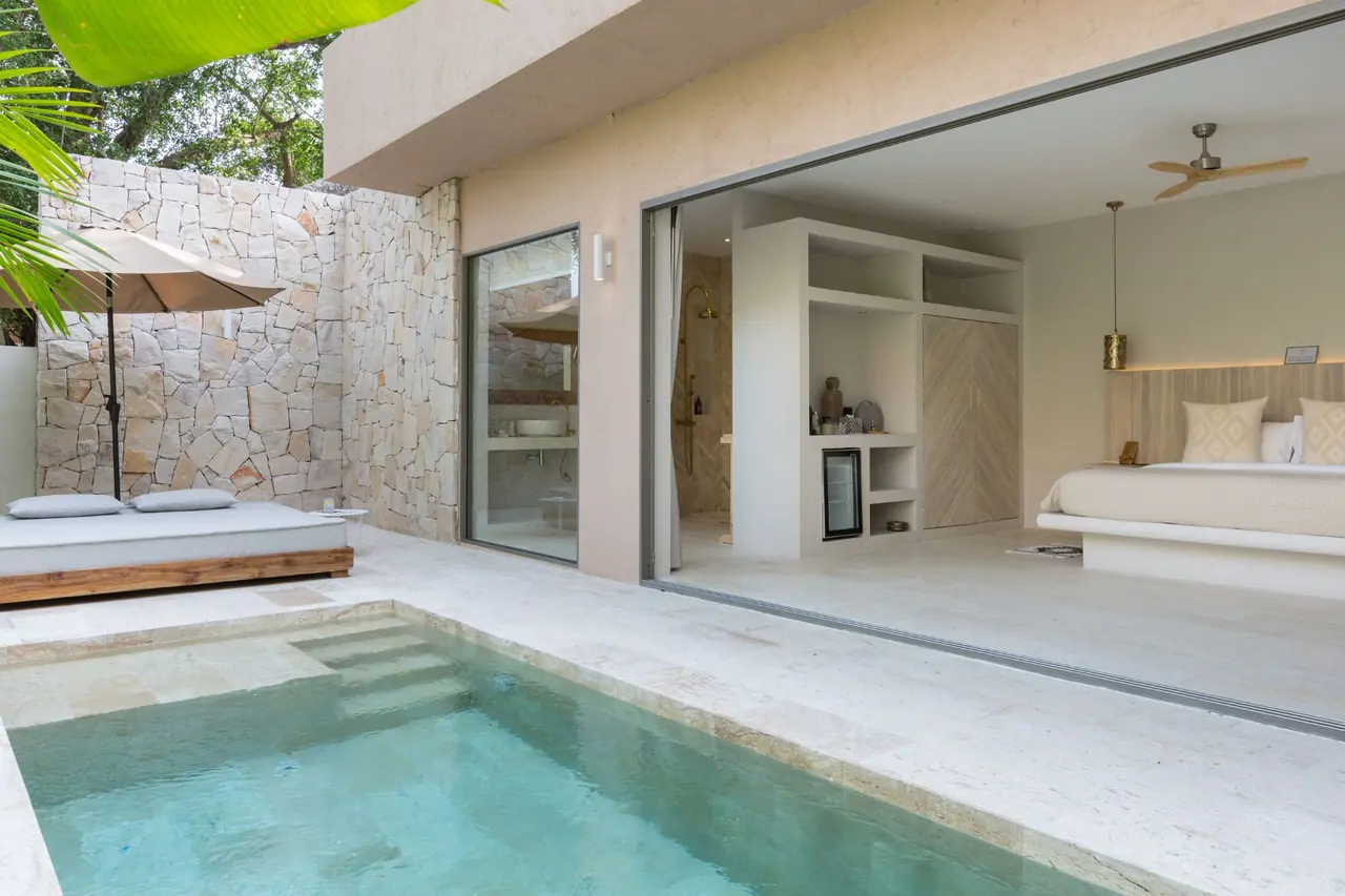 Plunge pool and daybed under a parasol in front of glass doors opened wide onto the bedroom.